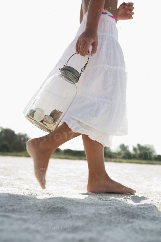 Girl on beach carrying jar of shells. Date : 2008