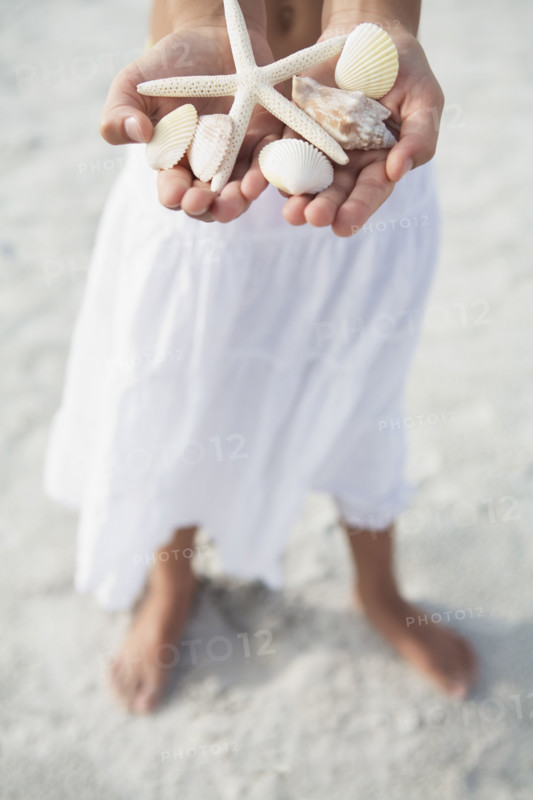 Girl on beach holding delicate starfish and shells. Date : 2008