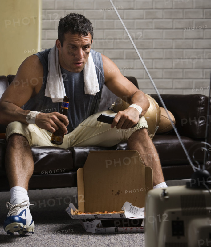 Football player watching game on sofa with beer. Date : 2008