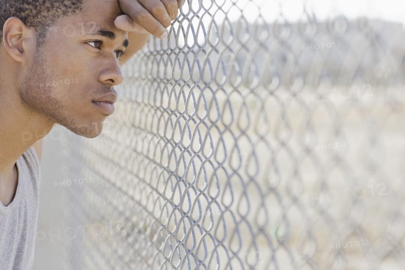 Young man leaning against chain-link fence. Date : 2008