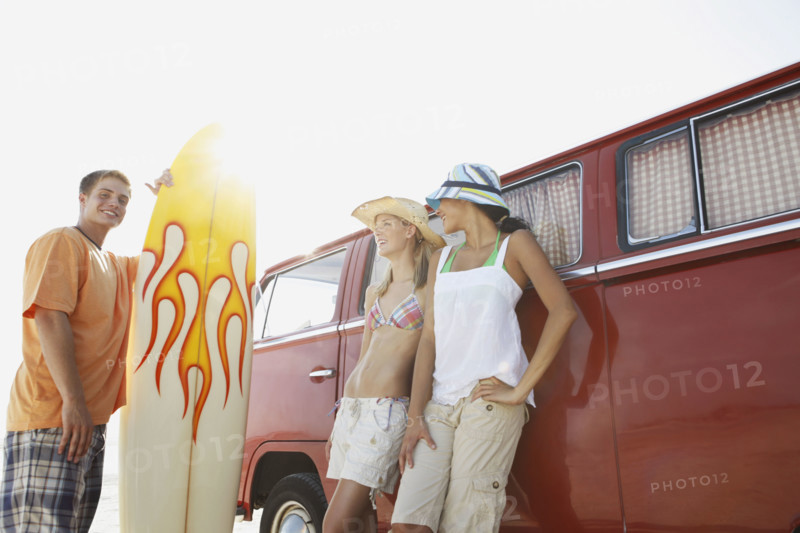 Young man with surfboard and women leaning against van. Date: 2008