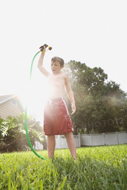 Boy spraying himself with hose in backyard. Date: 2008