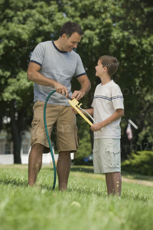 Boy helping father with sprinkler in backyard.