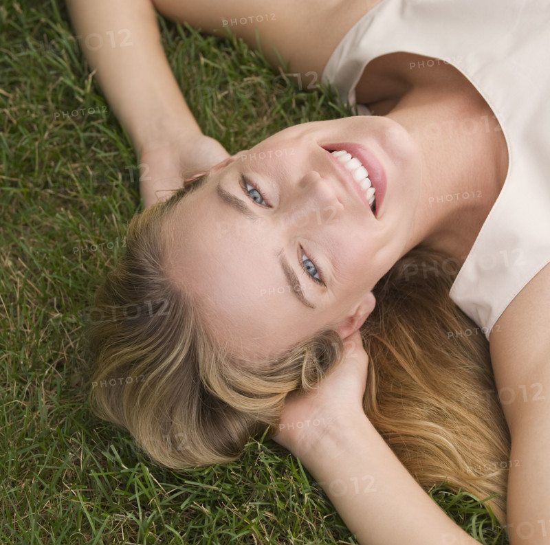 Woman laying in grass with hands behind head.