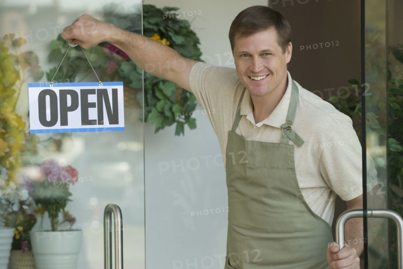 Man hanging open sign in flower shop window.