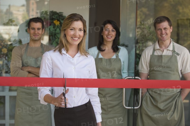 Small business owner cutting red ribbon at grand opening.