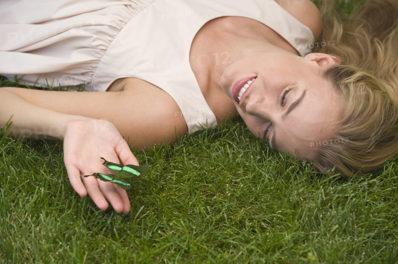 Woman laying on grass holding green butterfly.