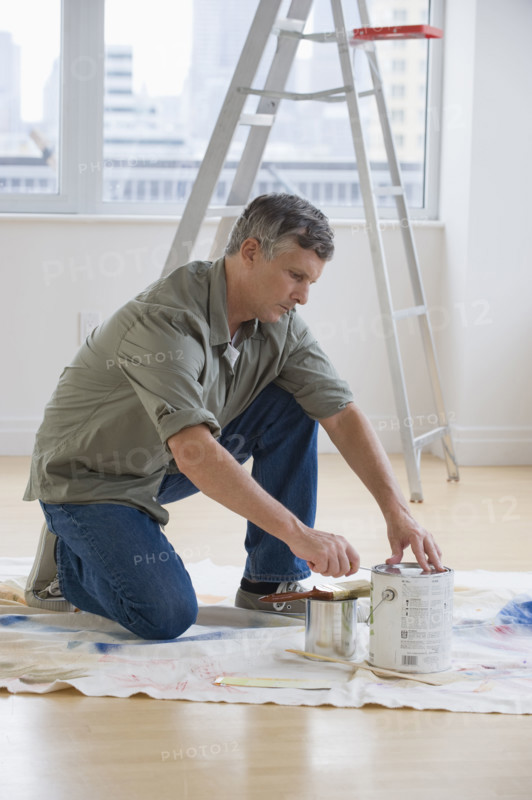 Man opening paint cans on drop cloth.