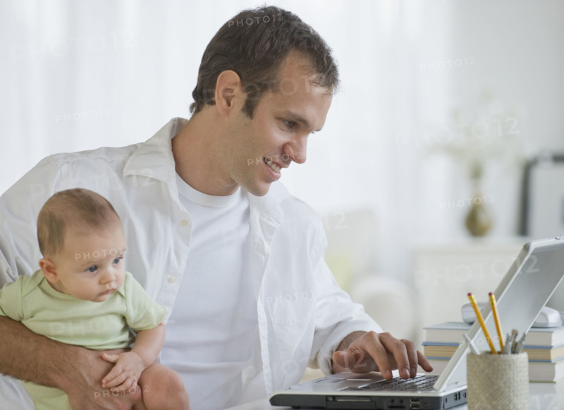 Father working on laptop and holding son.