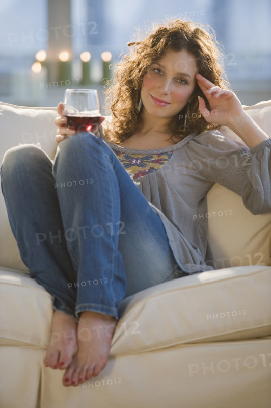 Portrait of woman with red wine sitting on sofa.