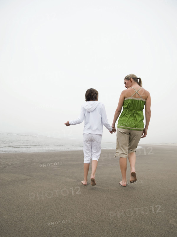 Mother and daughter holding hands and walking on beach. Date : 2008