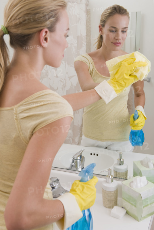 Woman cleaning mirror in bathroom.