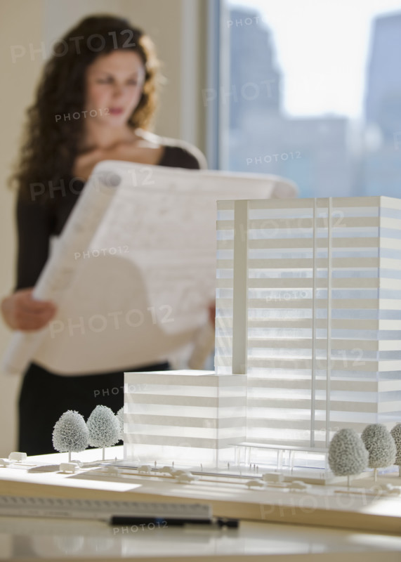 Architect viewing blueprints near building model.