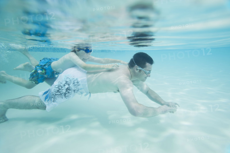 Boy swimming on father’s back underwater. Date : 2008