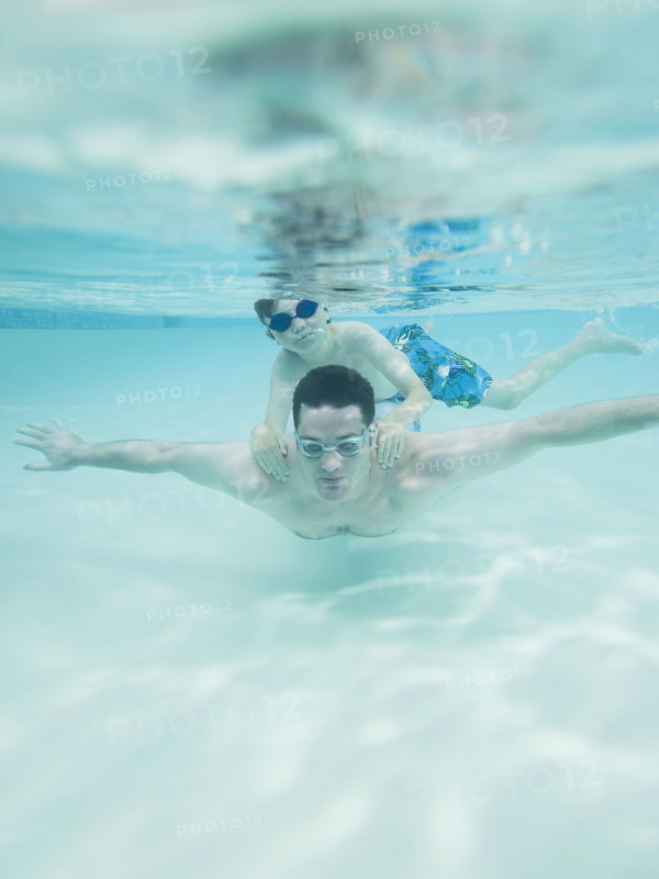 Boy swimming on father’s back underwater. Date : 2008