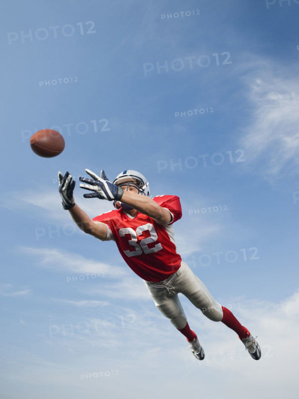 Football player in mid-air reaching for football. Date: 2008