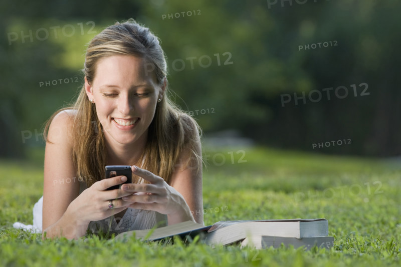 College student reading in grass and text messaging. Date : 2008