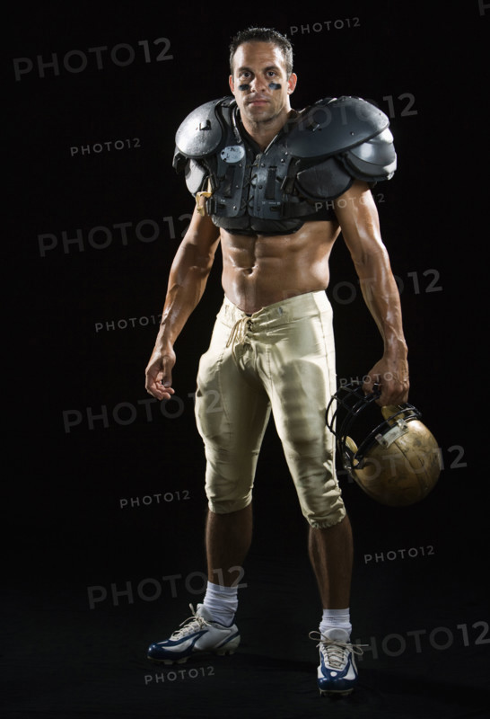 Football player wearing protective gear and holding helmet. Date : 2008