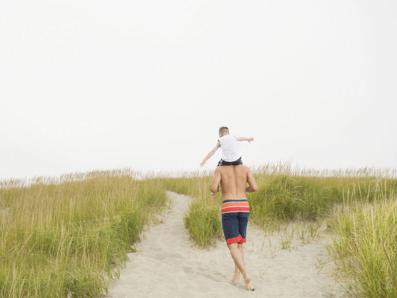 Father carrying son on shoulders at beach. Date: 2008