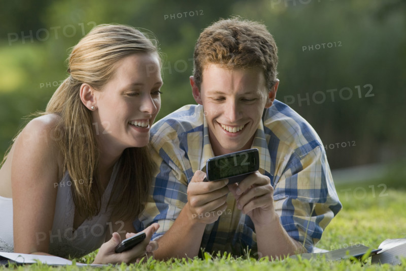 College students laying in grass with books and cell phones. Date : 2008