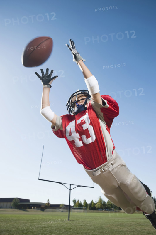 Football player in mid-air reaching for football. Date: 2008