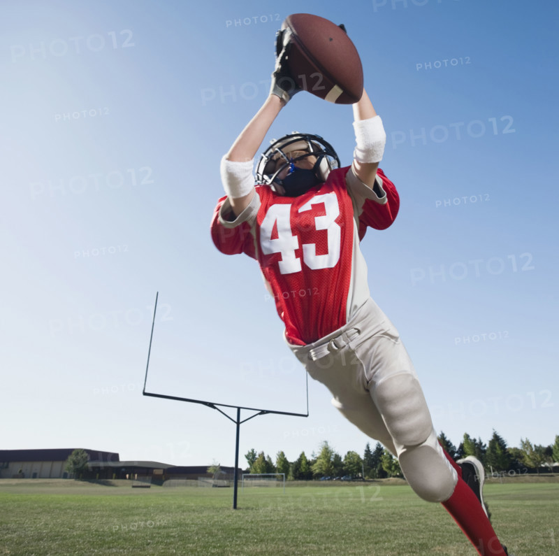 Football player in mid-air reaching for football. Date: 2008