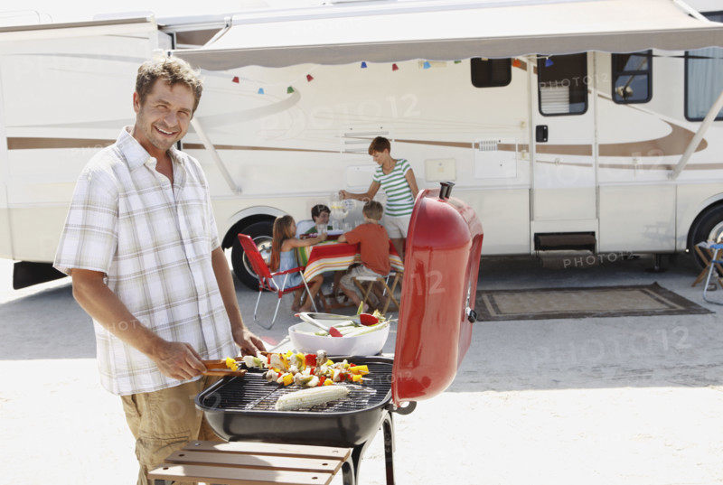 Man barbecuing with family and motor home in background. Date : 2008