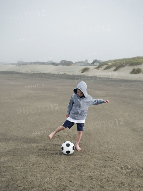 Boy kicking soccer ball on beach. Date: 2008
