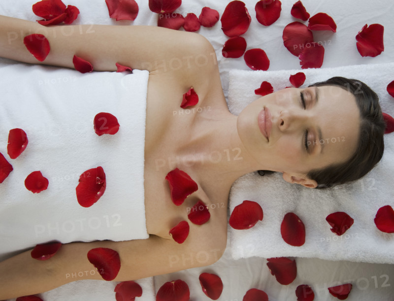 Woman covered in flower petals laying on massage table.