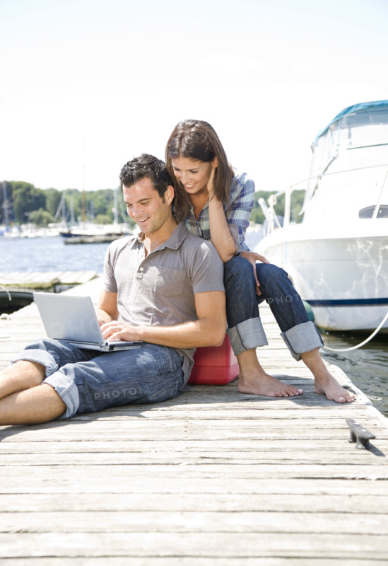 Couple using laptop on dock. Date : 2008