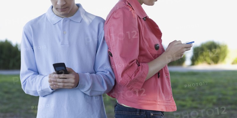 Young couple text messaging outdoors. Photographe : PT Images