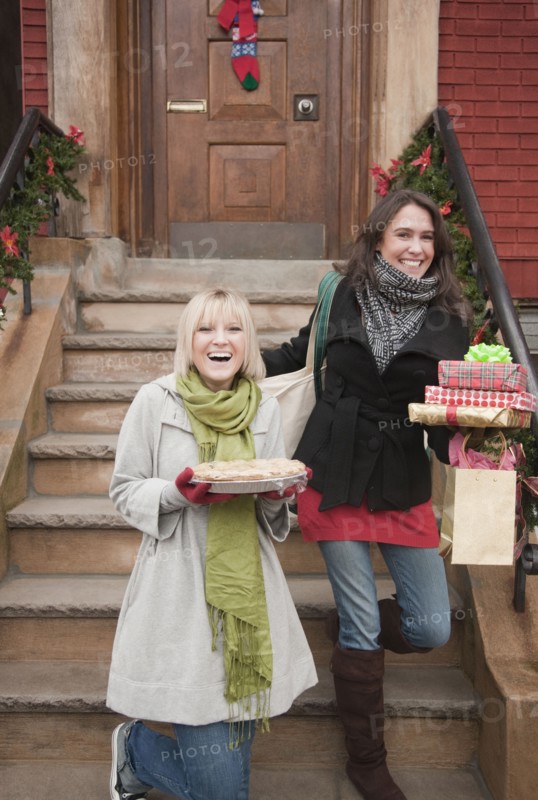 Women carrying Christmas gifts on front stoop. Photographe : Jamie Grill