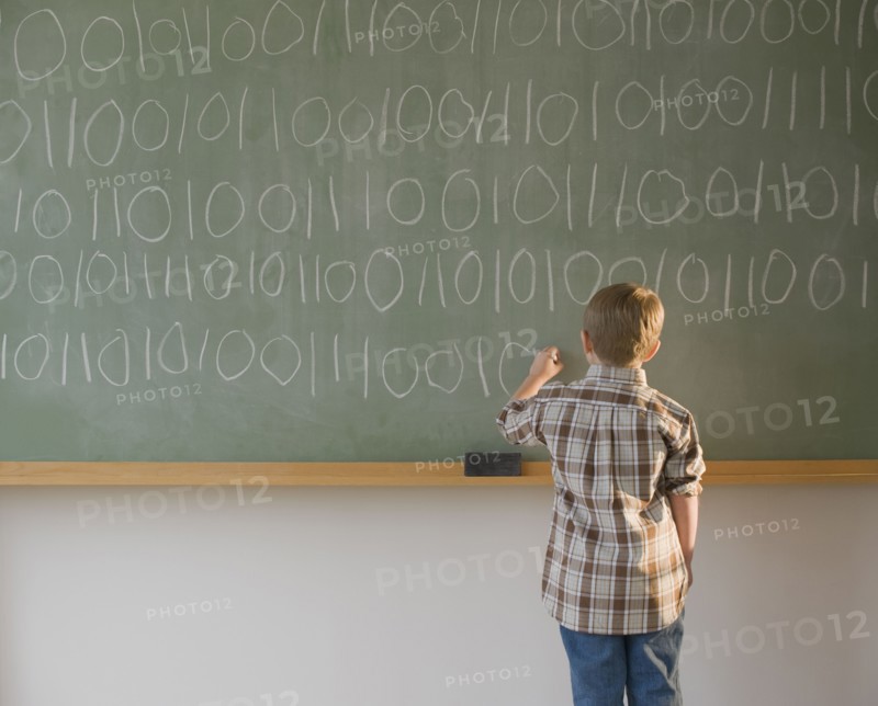 Boy writing binary code on blackboard.