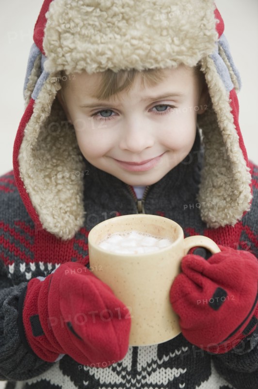 Boy in warm hat drinking hot chocolate.