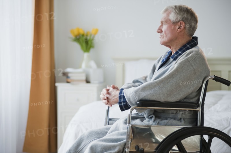 Senior man in wheelchair looking out window.