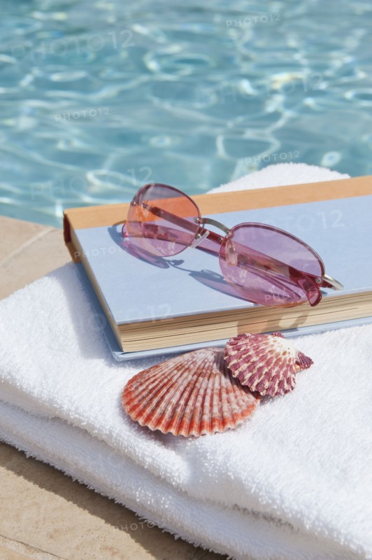 Book and sunglasses by swimming pool.