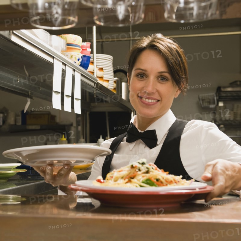 Waitress taking plates of food from kitchen.