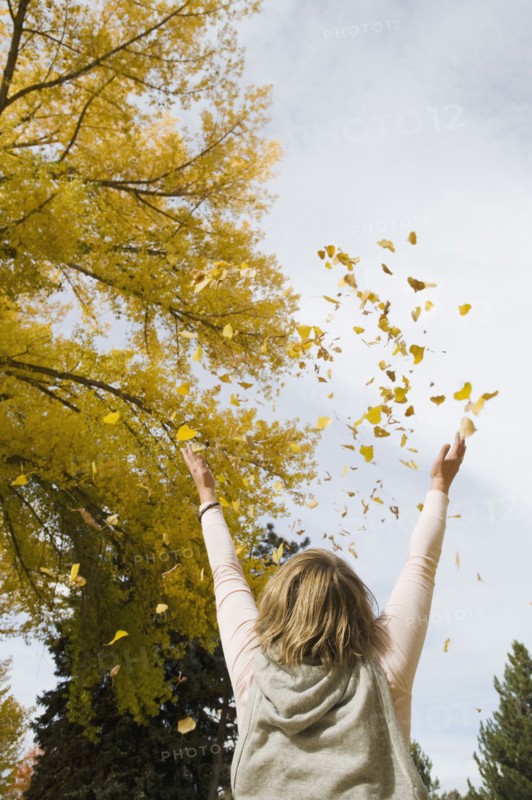 Woman throwing autumn leaves in air.