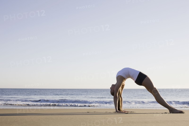 Woman doing yoga on beach. Photographe : PT Images