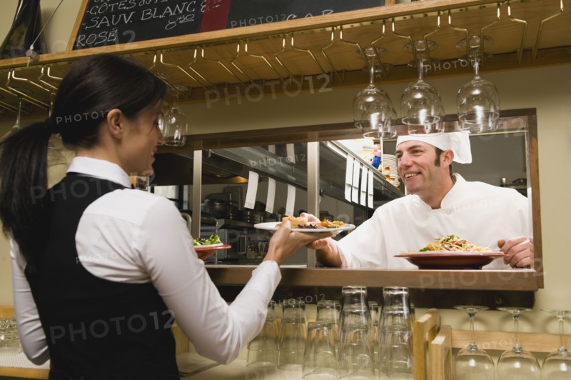 Chef giving waitress plates of food.