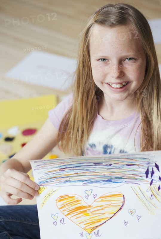 Girl (10-12) sitting on floor and showing her picture, portrait. Photographe : Sarah M. Golonka