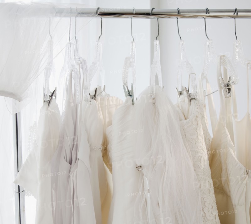 Row of wedding dresses hanging on clothes rail. Photographe : Jamie Grill