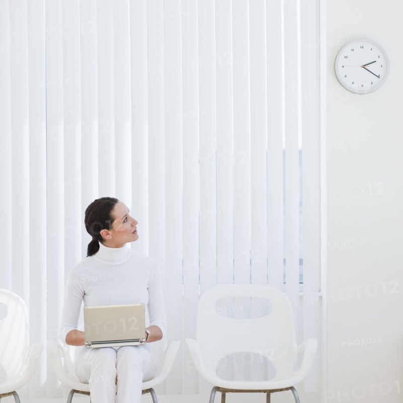 Businesswoman looking at clock in waiting room.