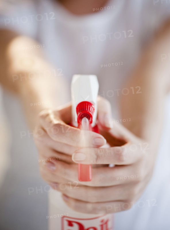 Woman holding and spraying cleaning fluid, close-up.