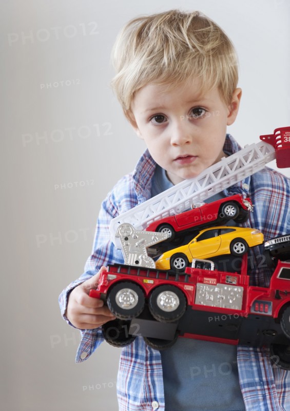 Portrait of boy (3-4) holding toy fire engine and cars.