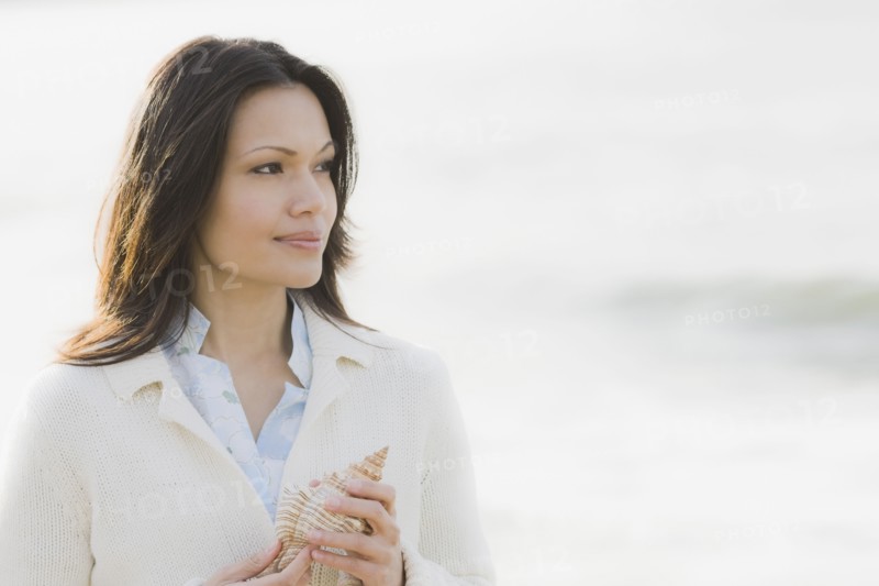 Woman holding shell by sea. Photographe : PT Images