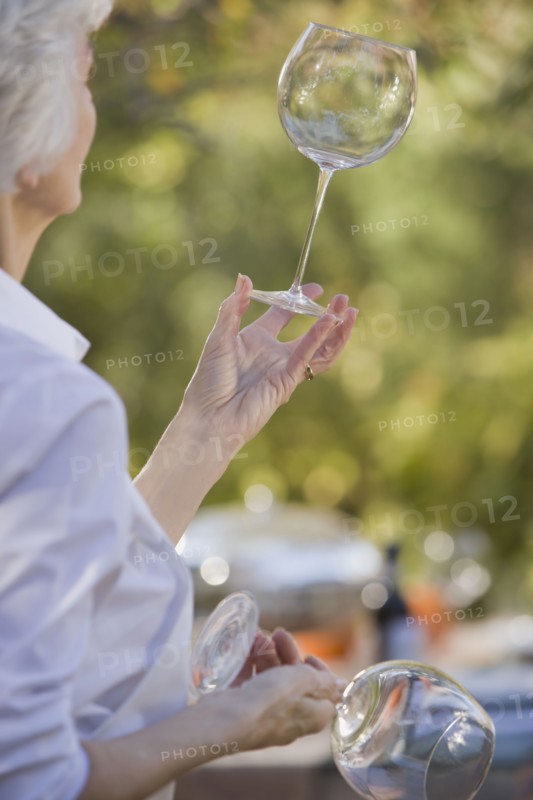 Senior woman standing in garden and examining wineglasses. Photographe : mark edward atkinson
