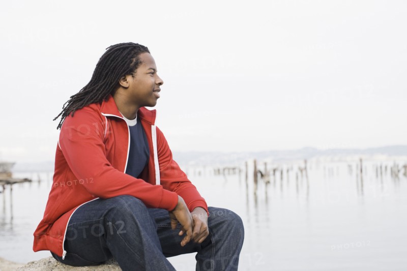 Teenage boy (16-17) with dreadlocks, sitting at waterfront, San Francisco, California, USA. Photographe : PT Images