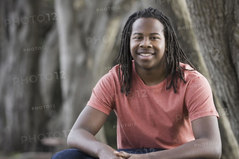 Portrait of teenage boy (16-17) with dreadlocks, sitting in park. Photographe : PT Images