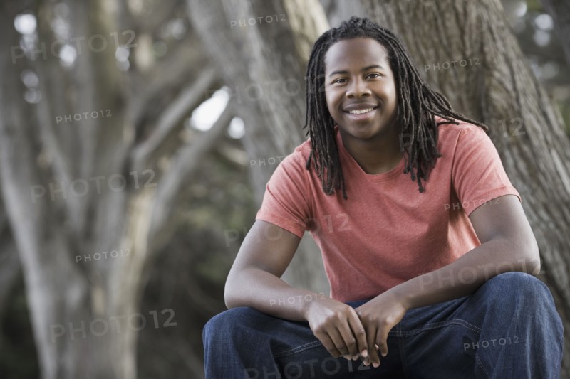 Portrait of teenage boy (16-17) with dreadlocks, sitting in park. Photographe : PT Images